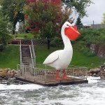 large pelican statue standing on a wide dock over a river